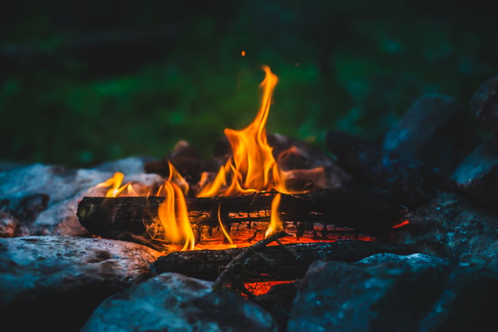 A campfire burning brightly with logs surrounded by rocks in a dark, outdoor setting.